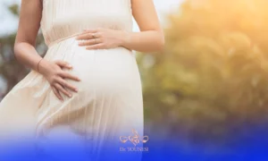 خانمی باردار با لباس سفید که دستان خود را روی شکمش قرار داده